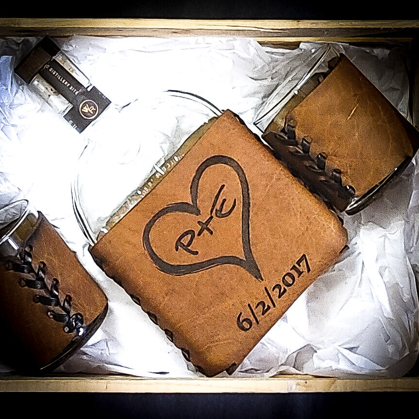 3 year anniversary leather whiskey set with heart-shaped logo and initials p plus einside with two whiskey glasses in a light brown tan 3-year wedding anniversary gift