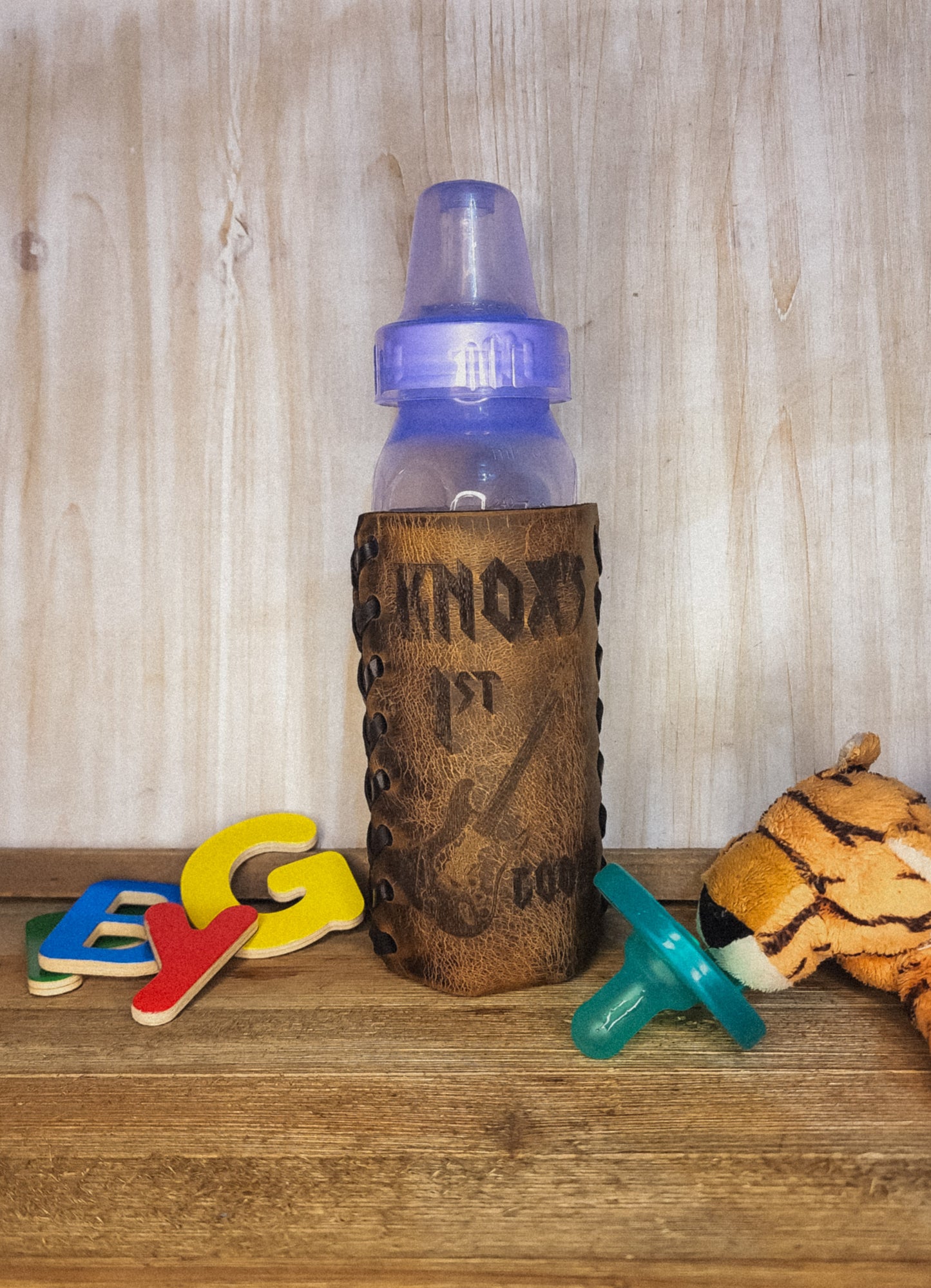 Personalized leather baby bottle koozie with text Knox and an image of a guitar perfect gift for baby showers for boys